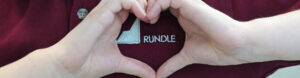 A Rundle student shapes their fingers in a heart around the Rundle logo