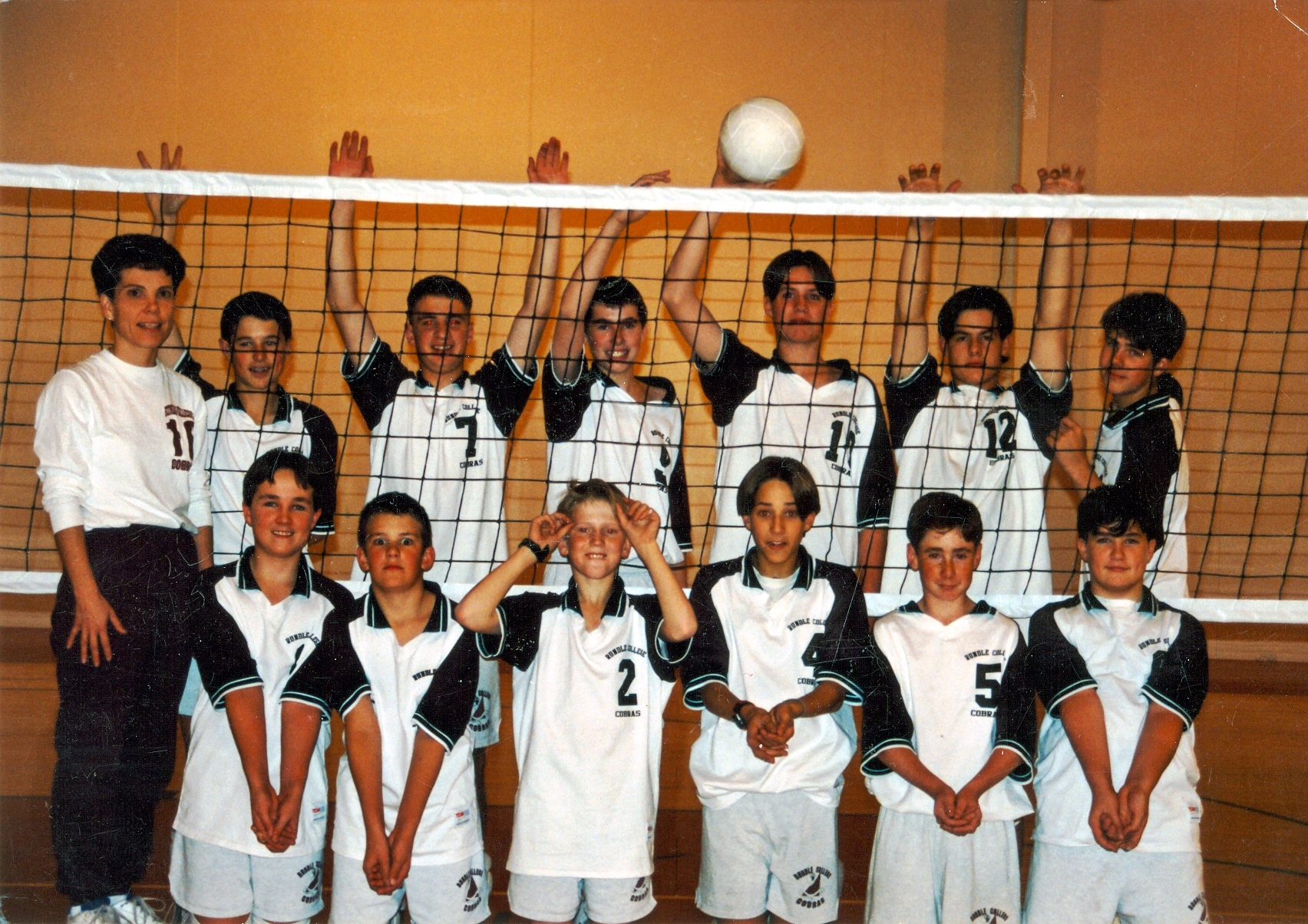 Rundle College Volleyball team posing as a team in front of a Volleyball net.